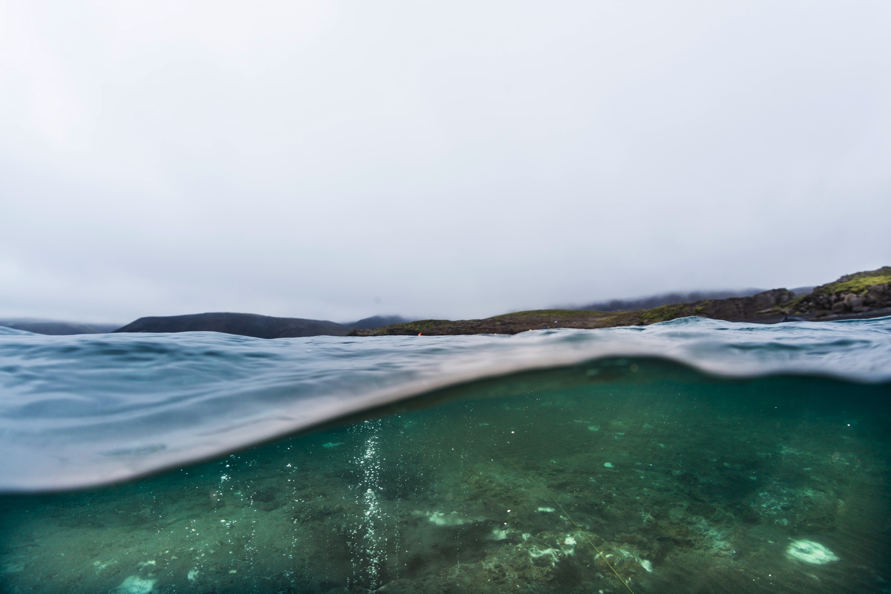split shot grey cloudy sky over Kleifarvatn with lavarock shore and green moss patches underwater bubbling sand bottom