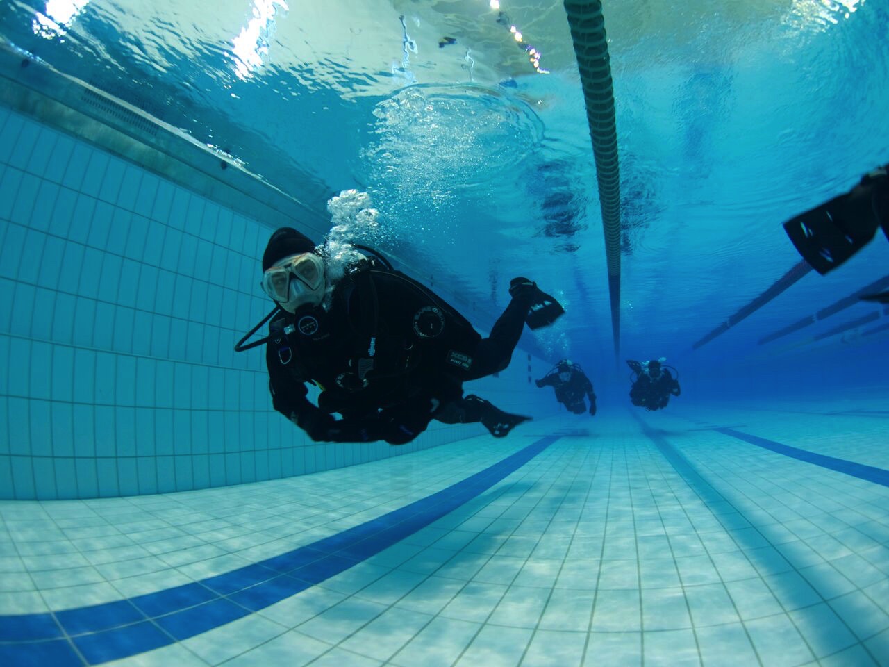 drysuit students approaching diving along swimming lane followed by two others in Afsvallalaug pool in Reykjavik