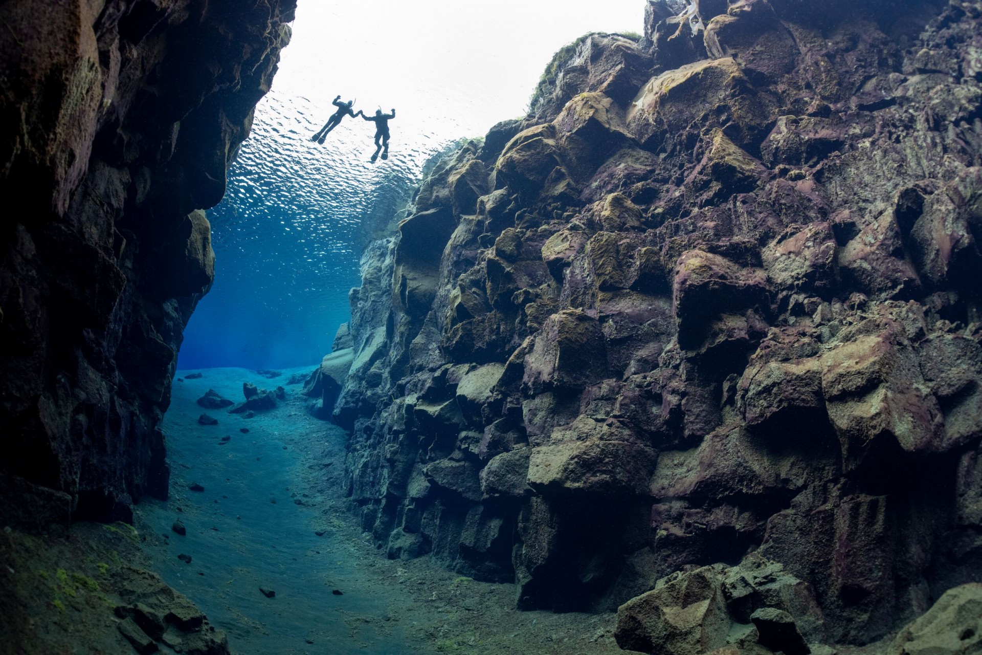 two snorkelers floating in the crystal clear Silfra fissure as seen from below