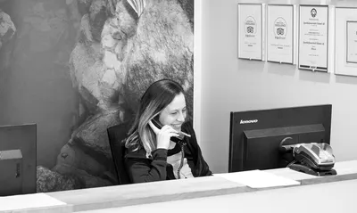 A smiling office angel answers the phone sitting at computer behind front desk in DIVE.IS shop in front of Silfra poster