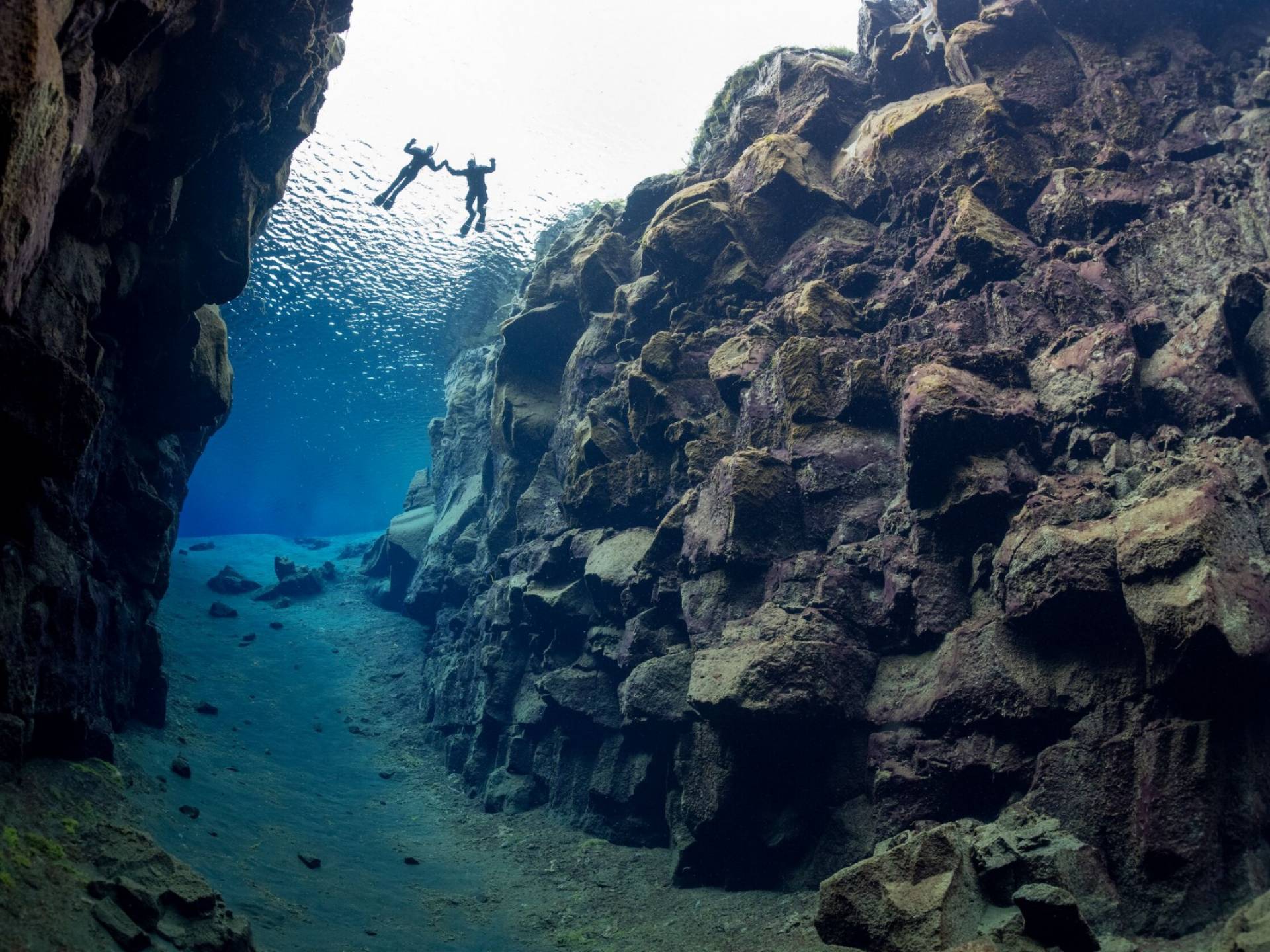 two snorkelers floating in the crystal clear Silfra fissure as seen from below