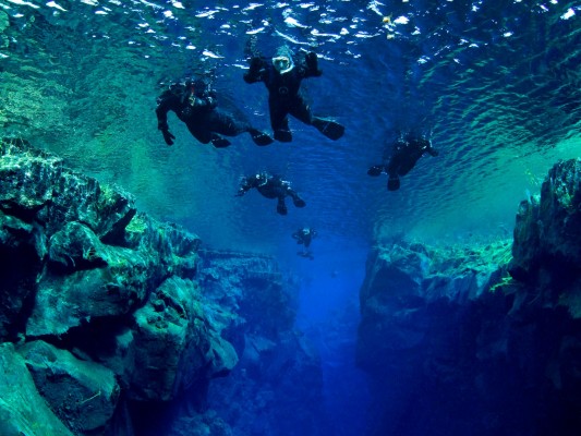 Snorkelers from below floating over Cathedral section in diverse aquamarine colors of Silfra fissure in Thingvellir