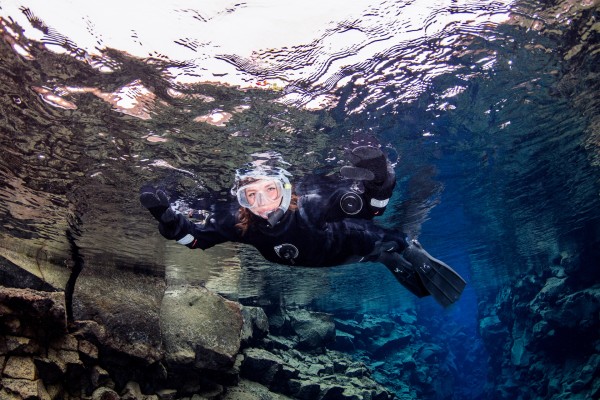 Happy Silfra snorkeler close up from beneath reflecting crystal water surface of Silfra hall in Thingvellir Iceland