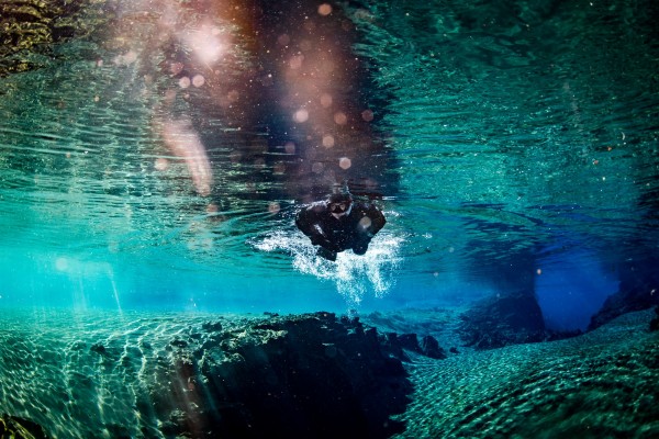 Snorkeler kicking in shallow passage from Silfra cathedral into lagoon with sunrays sparkling through crystal turquoise water