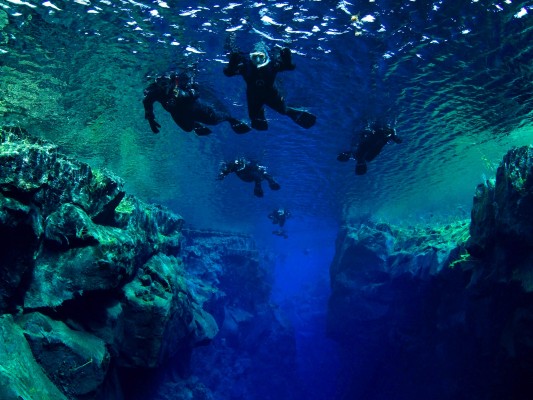 Snorkelers from below floating over Cathedral section in diverse aquamarine colors of Silfra fissure in Thingvellir