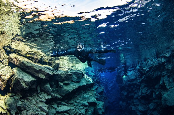 A group with snorkeler in forefront floating through deep crystal waters of Silfra Big Crack off entrance-platform